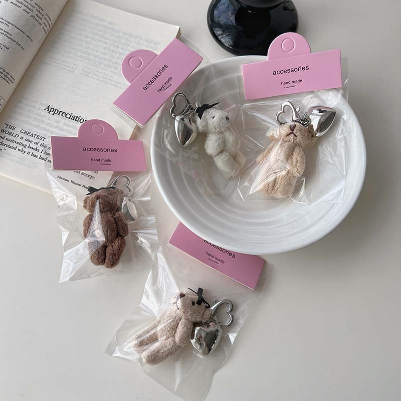 Plüss medve kulcstartó szív alakú medállal – rajzfilmszerű stílus, táskára akasztható dísz; anyag: textil; minta: medve; 2024 nyári kiadás; feldolgozás: félig manuális.