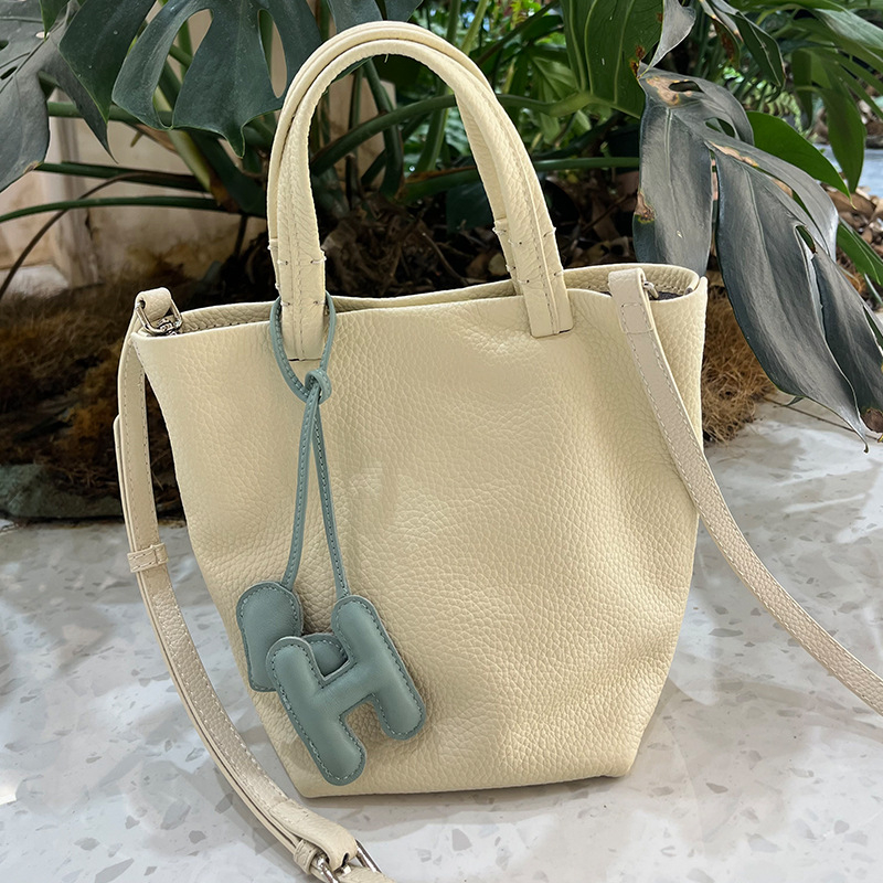 Geantă bucket din piele naturală cu închidere magnetică, textură moale, buzunare interne pentru telefon și card de identificare, design urban minimalist