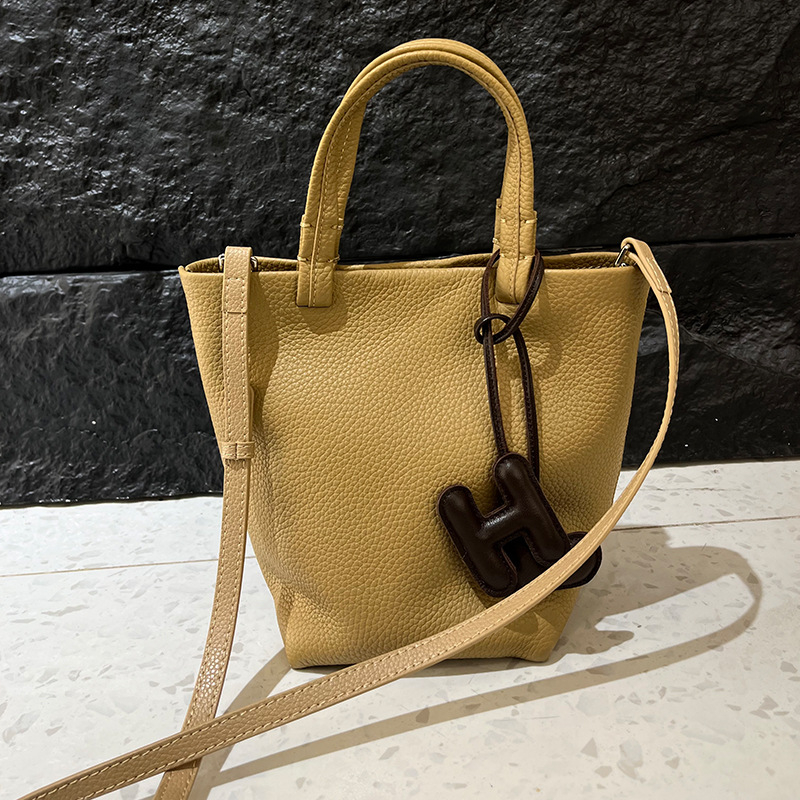 Geantă bucket din piele naturală cu închidere magnetică, textură moale, buzunare interne pentru telefon și card de identificare, design urban minimalist