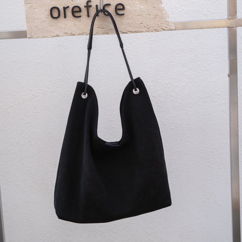 Nubukinės odos kibiro formos delninė pečių su minkšta rankena, matinė apdaila, poliesterio-paminkštintas pamušalas, vidinės kišenės telefonui ir dokumentams, ruduo 2025