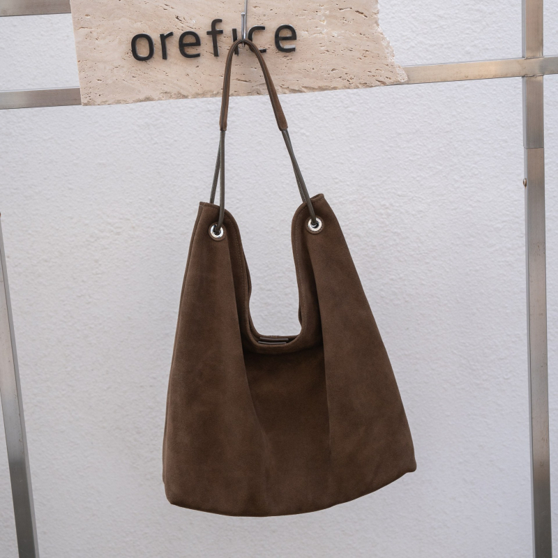 Nubukinės odos kibiro formos delninė pečių su minkšta rankena, matinė apdaila, poliesterio-paminkštintas pamušalas, vidinės kišenės telefonui ir dokumentams, ruduo 2025