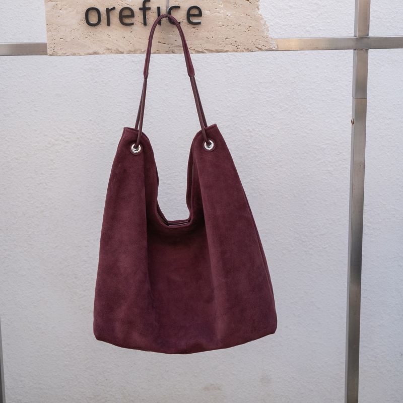 Nubukinės odos kibiro formos delninė pečių su minkšta rankena, matinė apdaila, poliesterio-paminkštintas pamušalas, vidinės kišenės telefonui ir dokumentams, ruduo 2025