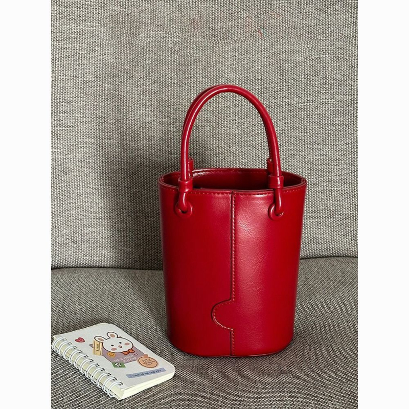 Crvena bucket torba s remenom za nošenje preko tijela i ručnim držalom, elegantna i svestrana