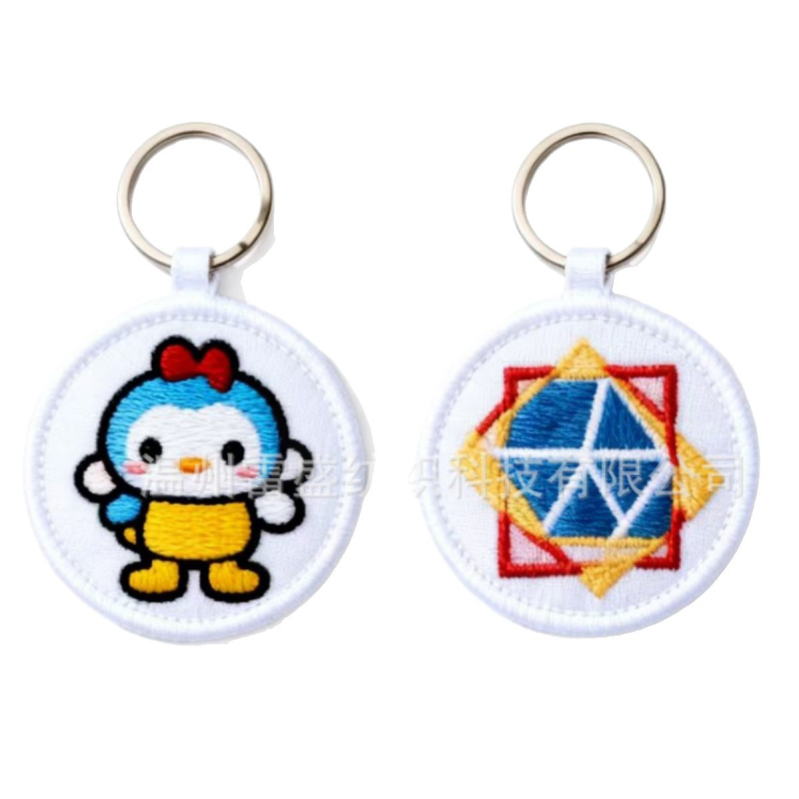 Siuvinėtas raktų pakabukas su karikatūrų raštu, netaisyklingos formos; medžiagos: audinys, poliesterio siūlas, PU; procesai: siuvinėtas raktų pakabukas, siuvinėta knygos žymeklis, siuvinėta mažytė maišytė