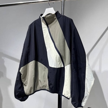 Ženska windbreaker jakna s dijagonalnim plaktom i kontrastnim šavovima, slobodan kroj, srednja duljina, polu-visoki ovratnik, dugi rukavi, poliester 70–80%