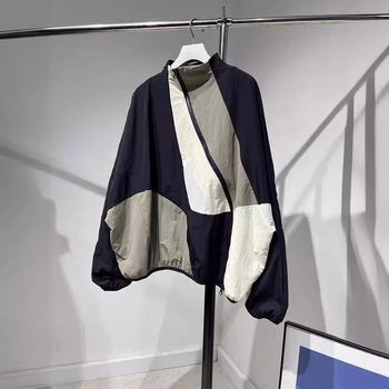 Ženska windbreaker jakna s dijagonalnim plaktom i kontrastnim šavovima, slobodan kroj, srednja duljina, polu-visoki ovratnik, dugi rukavi, poliester 70–80%