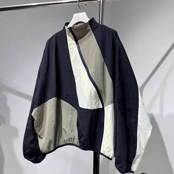 Ženska windbreaker jakna s dijagonalnim plaktom i kontrastnim šavovima, slobodan kroj, srednja duljina, polu-visoki ovratnik, dugi rukavi, poliester 70–80%