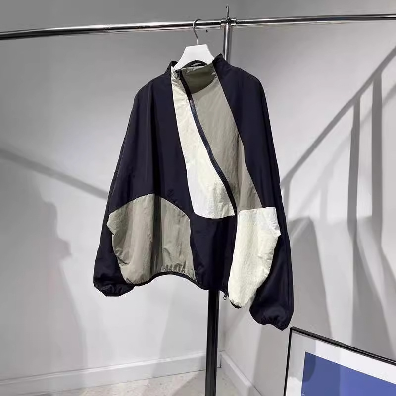 Ženska windbreaker jakna s dijagonalnim plaktom i kontrastnim šavovima, slobodan kroj, srednja duljina, polu-visoki ovratnik, dugi rukavi, poliester 70–80%