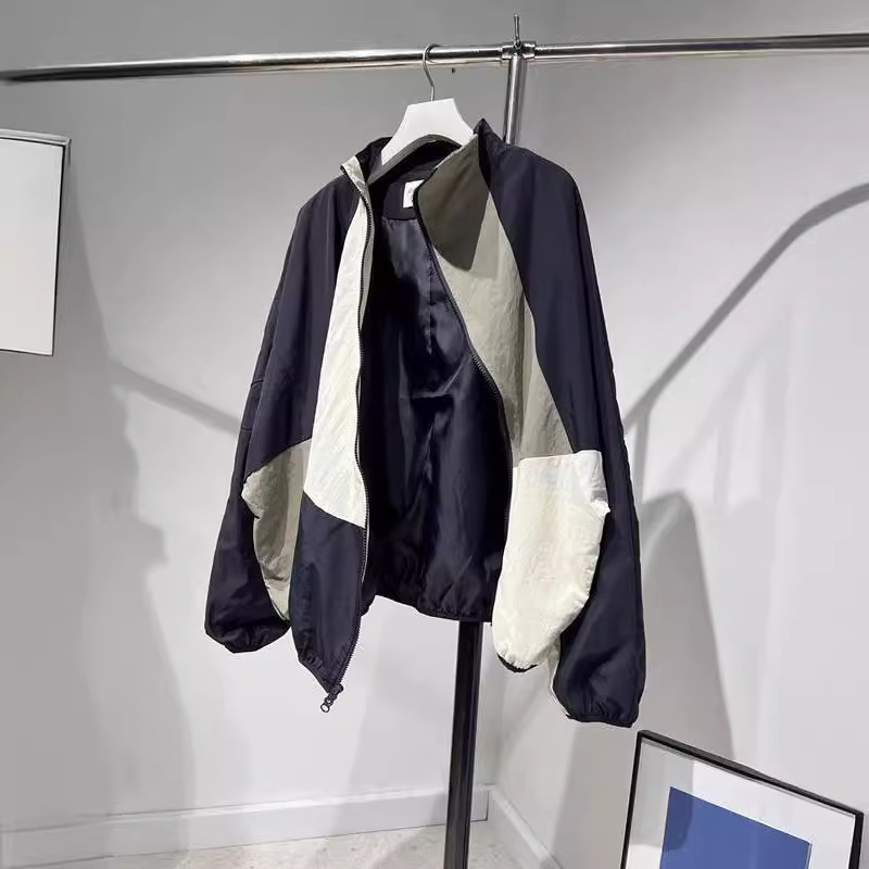 Ženska windbreaker jakna s dijagonalnim plaktom i kontrastnim šavovima, slobodan kroj, srednja duljina, polu-visoki ovratnik, dugi rukavi, poliester 70–80%