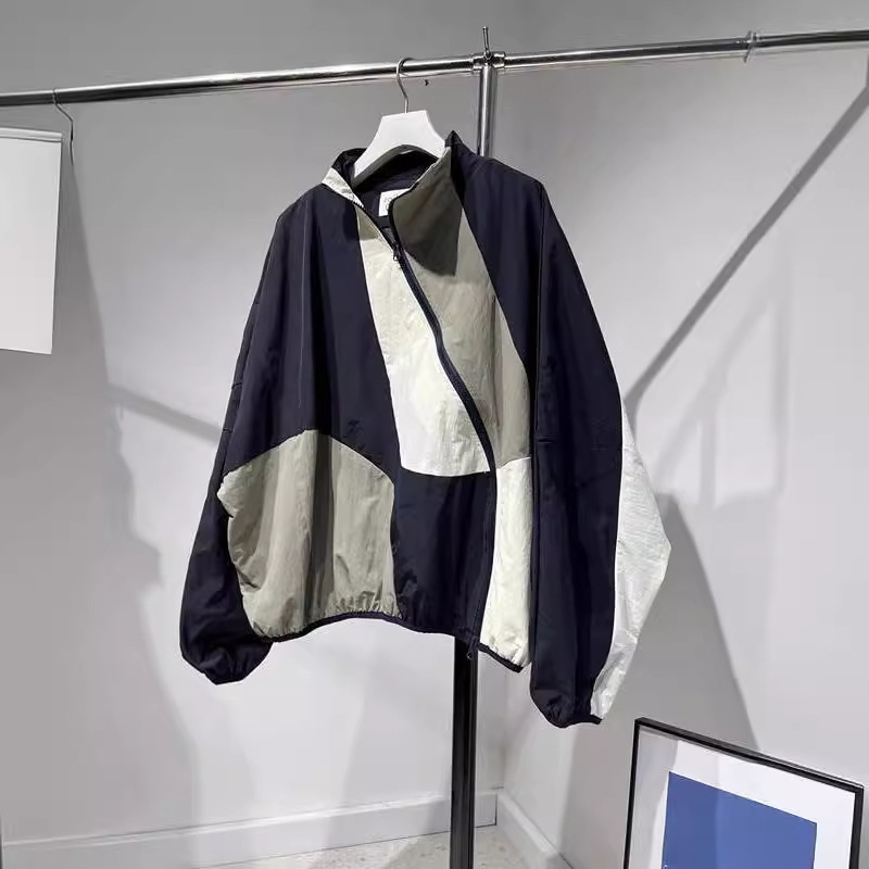 Ženska windbreaker jakna s dijagonalnim plaktom i kontrastnim šavovima, slobodan kroj, srednja duljina, polu-visoki ovratnik, dugi rukavi, poliester 70–80%
