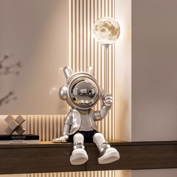 Sveķu karikatūras astronauta figūra, sēdošā pozā, kurā turo lampu; roku apglezīta, mūsdienīgs minimālisma stils, monētu krājējs