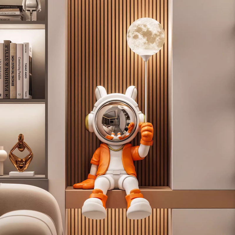 Sveķu karikatūras astronauta figūra, sēdošā pozā, kurā turo lampu; roku apglezīta, mūsdienīgs minimālisma stils, monētu krājējs