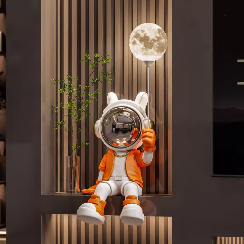 Sveķu karikatūras astronauta figūra, sēdošā pozā, kurā turo lampu; roku apglezīta, mūsdienīgs minimālisma stils, monētu krājējs