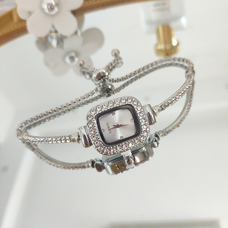 Ženski kvarcni sat s dekorativnim kamenčićima i svjetskim vremenom; metalno kućište i kaiš, okrugli brojčanik, leptir kopča