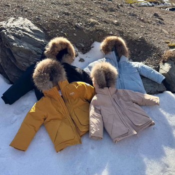 Meitenēm paredzēta pūkaina jaka ar kapuci – ar augstu apkakli, biezu pildījumu, 81–85% pīļu pūka, īss siluets