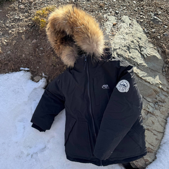 Meitenēm paredzēta pūkaina jaka ar kapuci – ar augstu apkakli, biezu pildījumu, 81–85% pīļu pūka, īss siluets