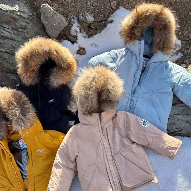 Meitenēm paredzēta pūkaina jaka ar kapuci – ar augstu apkakli, biezu pildījumu, 81–85% pīļu pūka, īss siluets