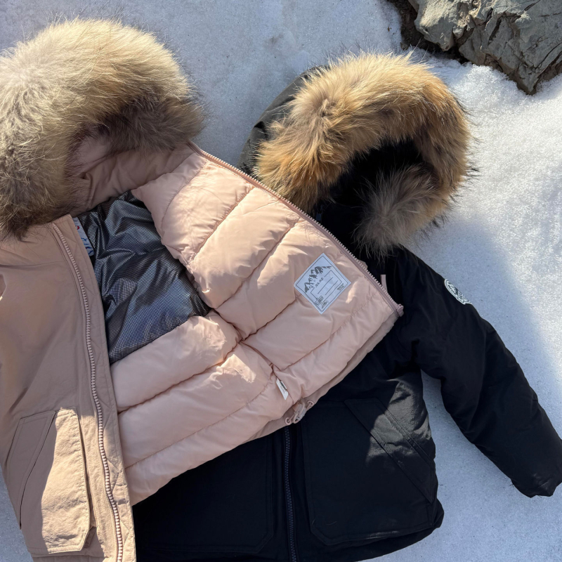 Meitenēm paredzēta pūkaina jaka ar kapuci – ar augstu apkakli, biezu pildījumu, 81–85% pīļu pūka, īss siluets