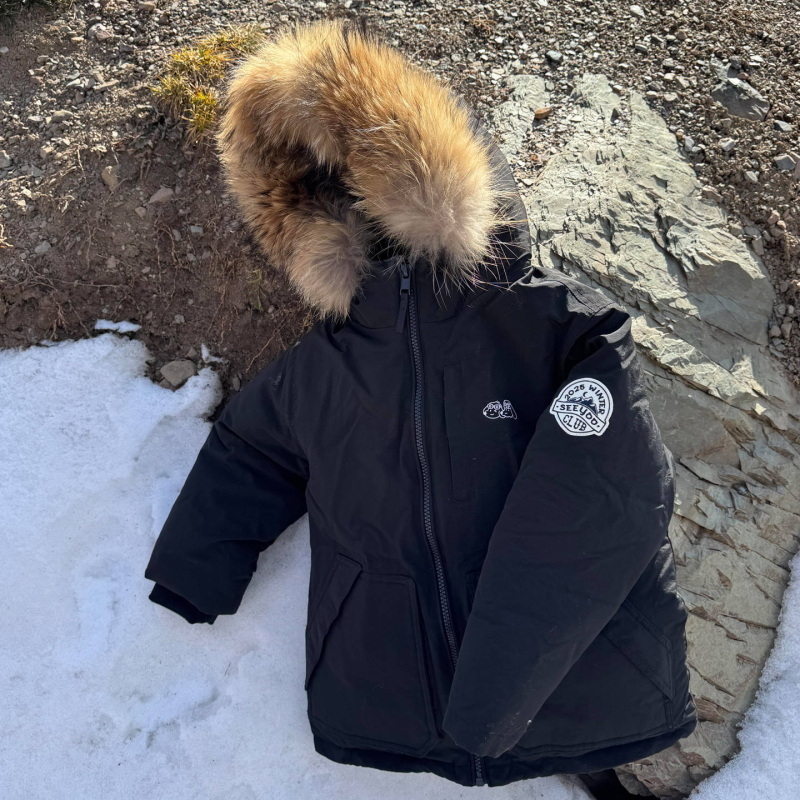 Meitenēm paredzēta pūkaina jaka ar kapuci – ar augstu apkakli, biezu pildījumu, 81–85% pīļu pūka, īss siluets