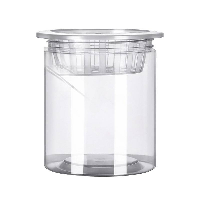 Caurspīdīgs plastmasas cilindrisks hydroponiskais pods sēklām un maziem augiem, stāvošs uz grīdas ar stādīšanas grozu, domāts mājas un dārza lietošanai