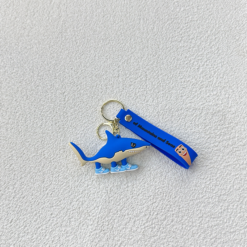 Breloc din PVC cu o figurină din lemn în formă de omuleț, purtând pantofi, și un pandantiv rechin