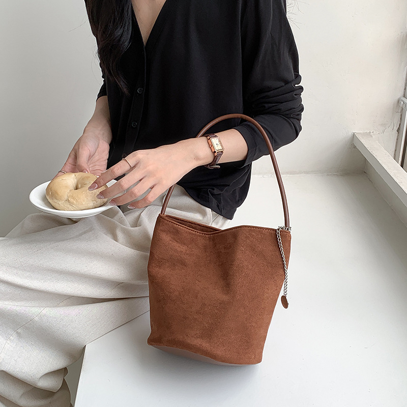 Suede bucket bag cilindričnog oblika s magnetskim zatvaračem; unutarnja džep s džepom na zatvarač, džep za mobitel i džep za ID.