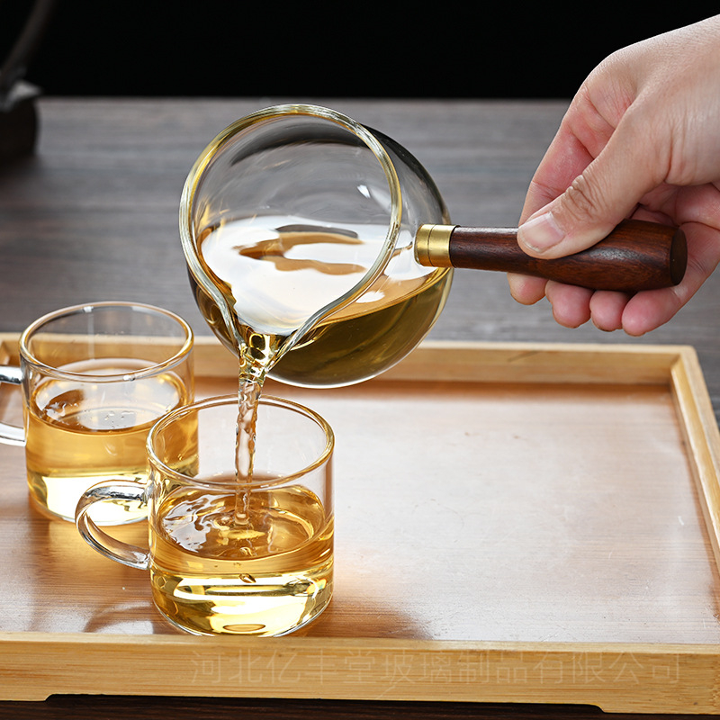 Set Gongfu pentru ceai din sticlă borosilicat rezistentă la căldură, cu mâner lateral din lemn; include cană de servire a ceaiului și ceașcă de distribuție egală.