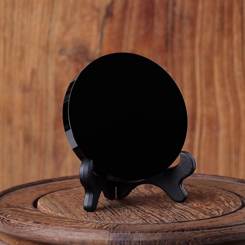 Prirodni obsidijan disk s glatkom crnom kristalnom površinom, ogledalo u obliku diska na crnoj podlozi