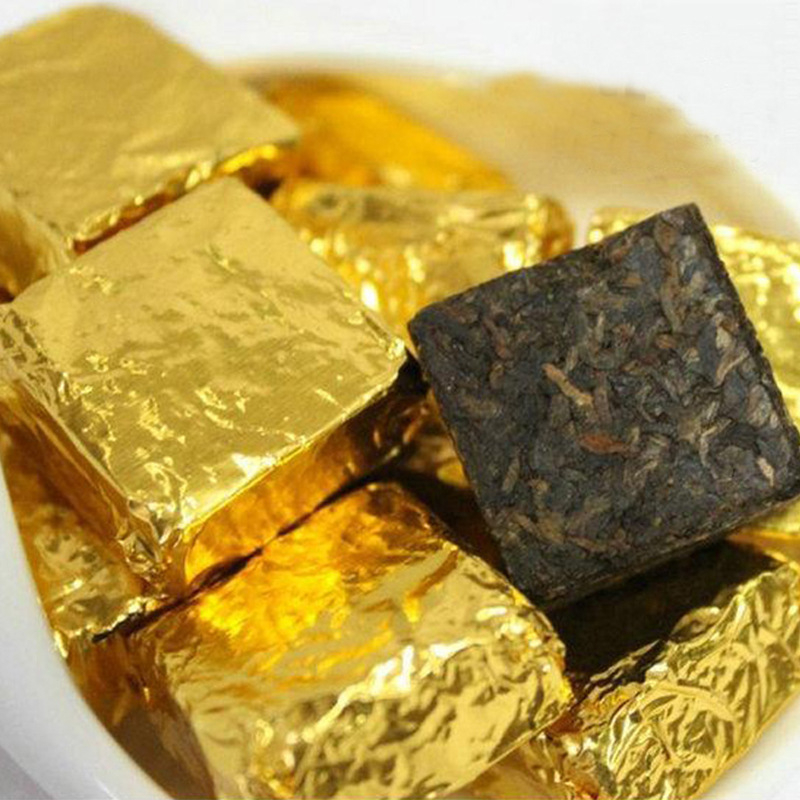 Zlatá hliníková baliaca fólia na bonbóny z čokolády a sezamových guličiek, lesklý povrch, jemný kosočtvercový vzor a textúra pomarančovej kôry