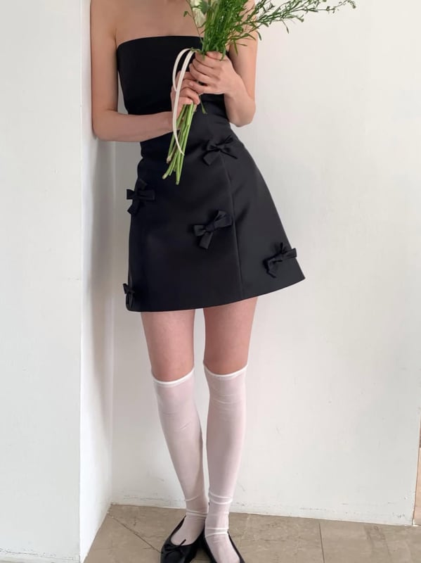Rochie de seară neagră din satin, scurtă, în stil Hepburn, fără bretele, decolteu pe umeri, funda; eleganță minimalistă de înaltă calitate
