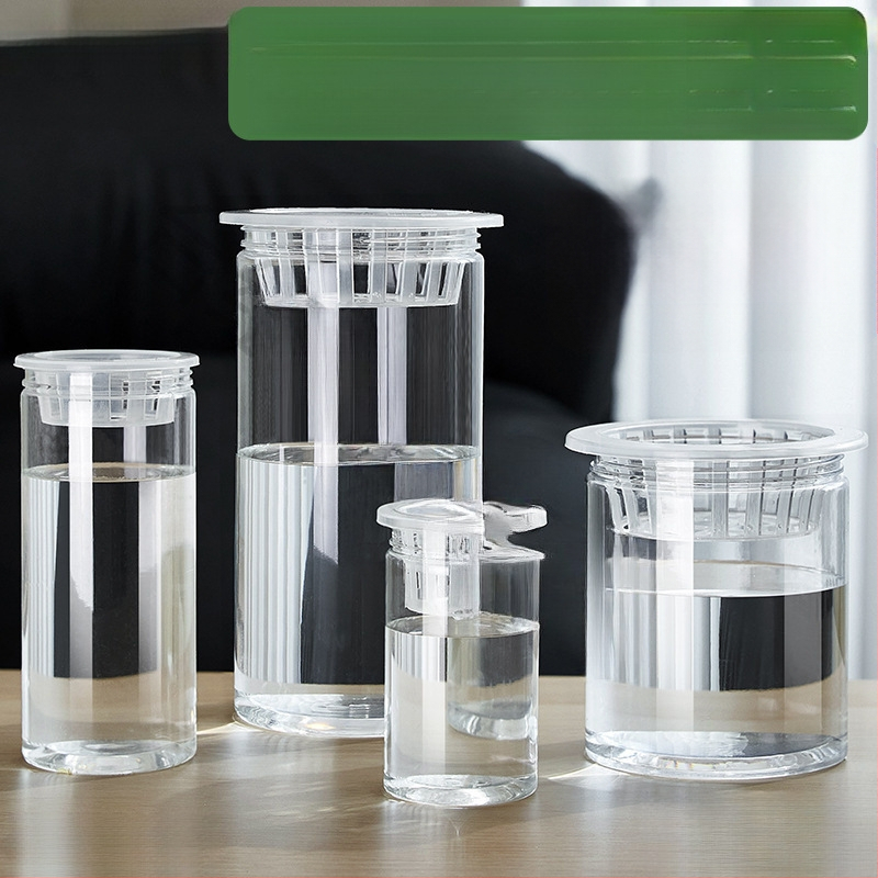 Caurspīdīgs plastmasas cilindrisks hydroponiskais pods sēklām un maziem augiem, stāvošs uz grīdas ar stādīšanas grozu, domāts mājas un dārza lietošanai